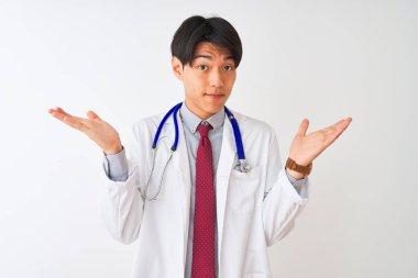 Ceket kravatı takan Çinli doktor ve steteskop izole edilmiş beyaz arka plan üzerinde bilgisiz ve elleri ve kolları havada kafası karışmış bir ifade. Şüphe kavramı.