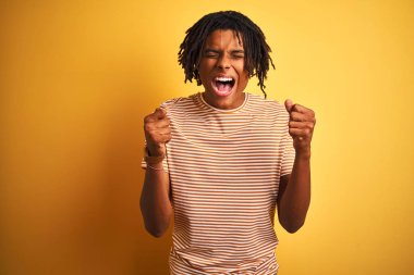 Sarışın, çizgili tişörtlü Afro bir adam. İzole edilmiş sarı arka planda duruyor. Kolları havada ve gözleri kapalı zaferi kutlarken gülümsüyor. Kazanan konsept.
