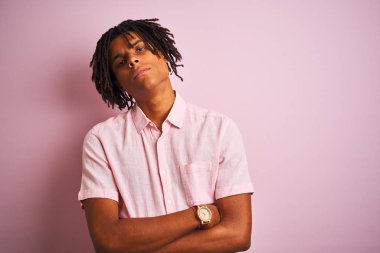 Zarif tişörtlü Afro-Amerikan bir adam soyutlanmış pembe arka plan üzerinde duruyor şüpheci ve gergin, yüzünde çapraz kollu tasvip etmeyen bir ifade. Negatif kişi.