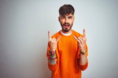 Turuncu süveter giyen genç adam izole edilmiş beyaz arka plan üzerinde duruyor çılgın bir ifadeyle el kaldırarak rock sembolü yapıyor. Müzik yıldızı. Ağır konsept.