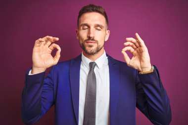 Mor izole edilmiş arka planda genç yakışıklı iş adamı rahatla ve gözün kapalı gülümse parmaklarınla meditasyon hareketi yap. Yoga konsepti.