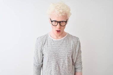 İzole edilmiş beyaz arka plan üzerinde çizgili tişört ve gözlük takan genç albino sarışın adam korku, şaşkınlık ifadesi ve heyecanlı yüz ifadesiyle dehşete düşmüş ve şok olmuştu..
