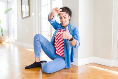 Afro saçlı güzel genç Afrikalı Amerikalı kadın, mutlu yüz ile eller ve parmaklar ile çerçeve yapma gülümseyen yerde oturuyor. Yaratıcılık ve Fotoğrafçılık konsepti.