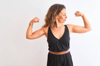 İzole edilmiş beyaz arka planda duran siyah günlük elbise giyen orta yaşlı bir kadın gururla gülümseyen kol kaslarını gösteriyor. Fitness konsepti.