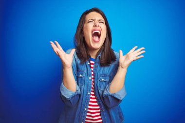Genç güzel esmer kadın mavi izole arka plan üzerinde rahat mavi kot ceket giyen kollarını kaldırdı ve kapalı gözleri heyecanlı çığlık ile başarı için deli ve deli kutluyor. Kazanan kavramı