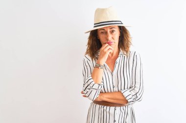 Orta yaşlı iş kadını çizgili elbise ve şapka giyip izole edilmiş beyaz arka plan üzerinde duruyor. Kollarını kavuşturup depresyondan sıkılmış ve yorgun görünüyor..