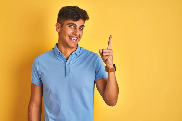 青いポロを身に着けている若いインド人男性は 成功したアイデアで指を指して孤立した黄色の背景の上に立っています 興奮し 第一番 — ストック写真