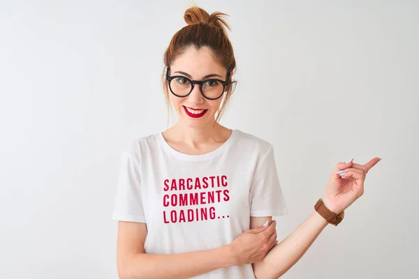 Redhead woman wearing funny t-shirt with irony comments over isolated white background very happy pointing with hand and finger to the side