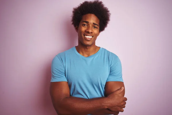 African american man with afro hair wearing blue t-shirt standing over isolated pink background happy face smiling with crossed arms looking at the camera. Positive person.