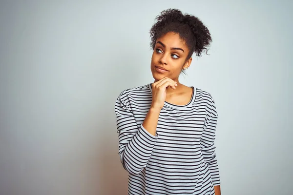 African american woman wearing navy striped t-shirt standing over isolated white background with hand on chin thinking about question, pensive expression. Smiling with thoughtful face. Doubt concept.