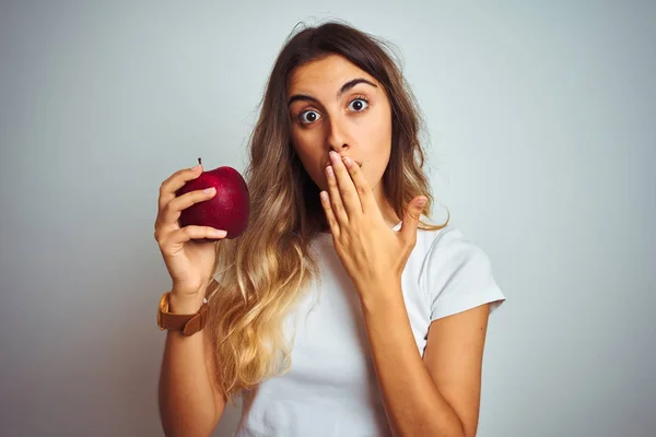 若い美しい女性の上に赤いリンゴを食べる灰色の隔離された背景カバー口で手を誤って恥とショックを受け 恐怖の表現 沈黙の中で怖がって 秘密の概念 — ストック写真