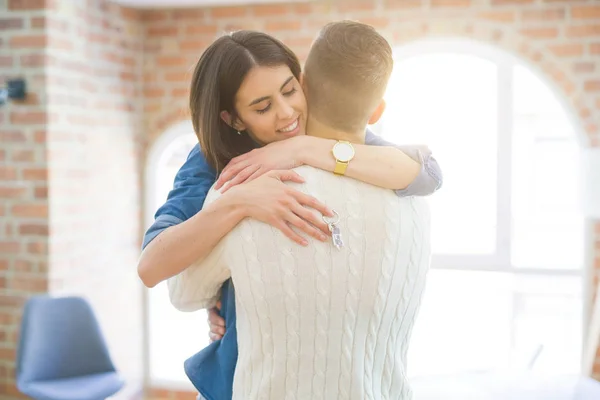 Casal jovem se mudando para uma nova casa, abraçando no amor mostrando chaves — Fotografia de Stock