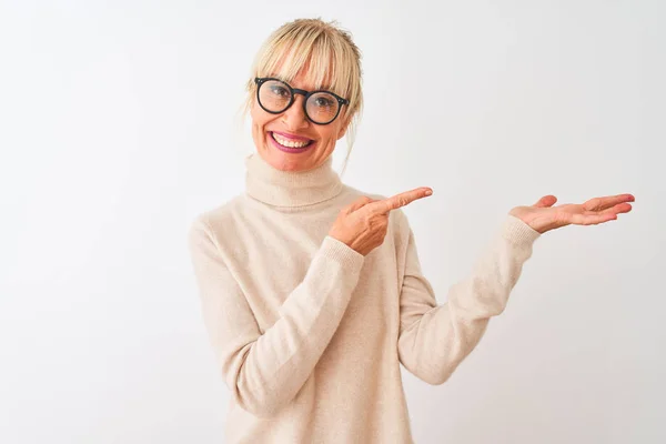 孤立した白い背景の上にタートルネックのセーターとメガネを身に着けている中年の女性は 手で提示し 指で指を指しながら カメラに驚き — ストック写真
