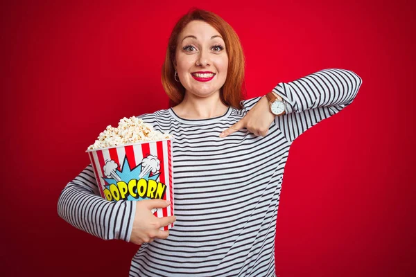 Fiatal Gyönyörű Vörös Hajú Eszik Popcorn Felett Piros Elszigetelt Háttér — Stock Fotó