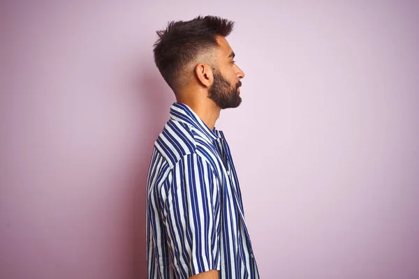 Young handsome indian man wearing summer striped shirt over isolated pink background looking to side, relax profile pose with natural face with confident smile.