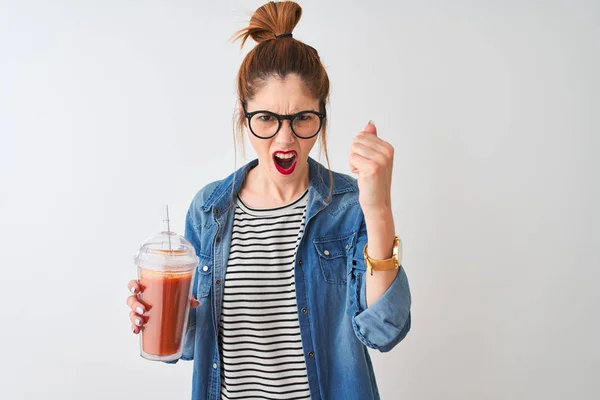 Beautiful redhead woman drinking smoothie of tomato over isolated white background annoyed and frustrated shouting with anger, crazy and yelling with raised hand, anger concept