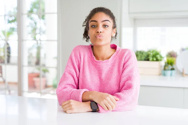 Beautiful african american woman with afro hair wearing casual pink sweater looking at the camera blowing a kiss on air being lovely and sexy. Love expression.