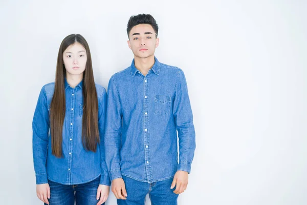 Beautiful young asian couple over white isolated background Relaxed with serious expression on face. Simple and natural looking at the camera.