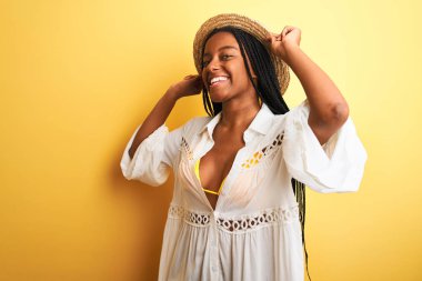 Güzel Afro-Amerikalı kız bikini ve yaz şapkası takıp mutlu gülümsüyor.