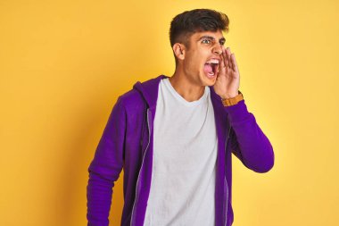 Mor eşofman üstü giyen genç Hintli adam izole edilmiş sarı arka planda durmuş el ele tutuşarak bağırıyor ve çığlık atıyordu. İletişim konsepti.