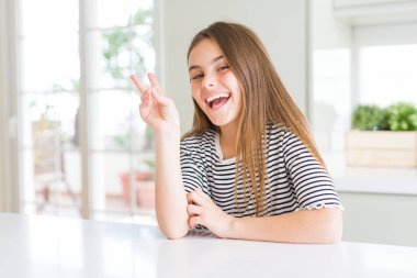 Beautiful young girl kid wearing stripes t-shirt smiling with happy face winking at the camera doing victory sign. Number two.