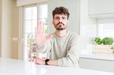Gündelik kazak giyen genç adam beyaz masada oturup avuç içiyle şarkı söylemeyi kesiyor. Yüzünde olumsuz ve ciddi bir jest olan uyarı ifadesi.