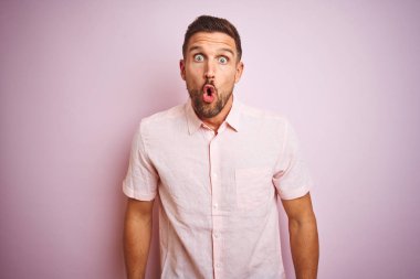 Pembe izole edilmiş arka planda zarif bir yaz gömleği giyen genç yakışıklı adam korku ve şaşkınlık dolu bir ifade ve heyecan dolu bir yüz ifadesiyle dehşete kapıldı..