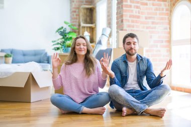 Genç güzel çift katta oturan yeni bir eve hareket ve gözleri parmakları ile meditasyon jest yapıyor kapalı gülümseyerek. Yoga konsepti.