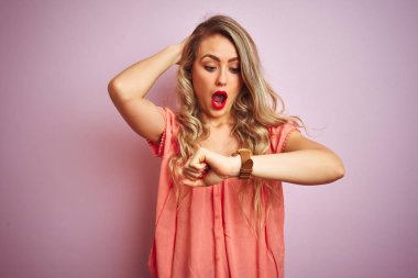 Young beautiful woman wearing t-shirt standing over pink isolated background Looking at the watch time worried, afraid of getting late