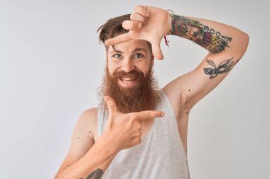 Genç kızıl İrlandalı adam izole gri arka plan üzerinde duran t-shirt giyen mutlu yüz ile elleri ve parmakları ile çerçeve yapma gülümseyerek. Yaratıcılık ve fotoğrafçılık konsepti.