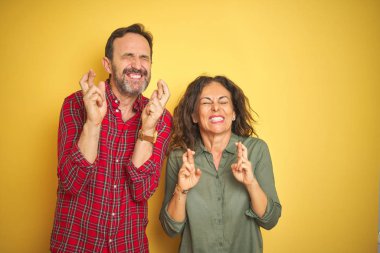 Izole sarı arka plan gesturing parmak üzerinde Güzel orta yaş çift umut ve gözleri kapalı gülümseyerek geçti. Şans ve batıl kavram.