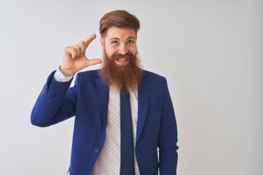 İzole edilmiş beyaz arka plan üzerinde duran takım elbiseli genç kızıl saçlı işadamı gülümsüyor ve el hareketleriyle küçük boy işareti yaparak kameraya bakıyor. Ölçü kavramı.