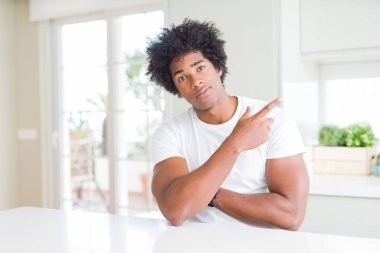 Genç Afro-Amerikalı, günlük beyaz tişörtler giymiş evde oturmuş, elini uzatarak reklamını yapıyor, ciddi ve sakin bir yüz ifadesi sergiliyor.