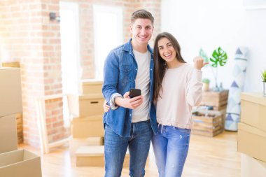 Güzel, genç bir çift yeni bir eve taşınıyor. Akıllı telefon kullanıyor ve gülümseyen bir gülümsemeyle baş parmağıyla onları işaret ediyor.