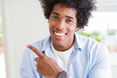 Yüzünde mutlu ve doğal bir ifadeyle elleri ve parmaklarıyla yüzünü gösteren yüzü gülen afro saçlı yakışıklı Afro Amerikalı adam.