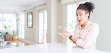 Afro saçlı, elleri açık, fotokopi alanını gösteren, gülümseyen mutlu bir gülümseme sunan Afro-Amerikan kadınının geniş açılı görüntüsü.