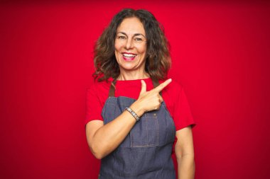 Kırmızı izole edilmiş arka planda önlük giyen orta yaşlı bir kadın. Yüzünde mutlu ve doğal bir ifadeyle el ve parmak uçlarını gösteren bir gülümseme var.