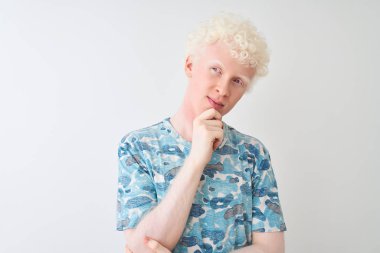 Sıradan tişörtler giyen genç albino bir adam izole edilmiş beyaz arka plan üzerinde duruyor ve elleri çenesinde soru sormayı düşünüyor, düşünceli bir ifade. Düşünceli bir yüzle gülümsüyor. Şüphe kavramı.