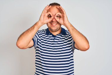 İzole edilmiş beyaz arka planda duran sıradan çizgili polo giyen genç bir adam dürbün gibi dil çıkartıyor, gözler parmaklarından bakıyor. Çılgın ifade.