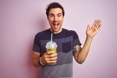 Dövmeli genç yakışıklı adam izole edilmiş pembe arka planda duruyor mutlu ve heyecanlı, kazanan yüz ifadesi zaferi büyük bir gülümsemeyle kutluyor ve ellerini kaldırıyor.