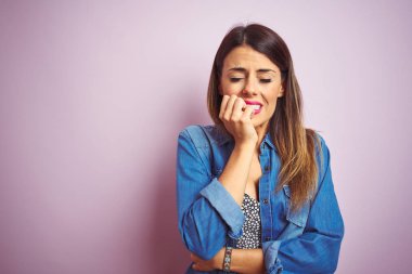 Genç güzel kadın pembe izole arka plan üzerinde duran stresli ve ağız tırnak ısırma elleri ile sinir görünümlü. Anksiyete sorunu.
