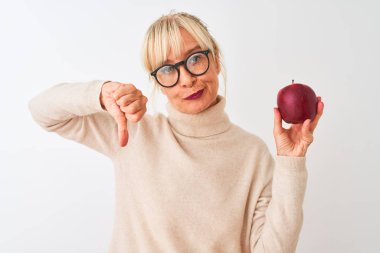 Orta yaşlı kadın, elinde elma gözlüğü, izole edilmiş beyaz arka planda duruyor. Kızgın yüzü var. Eksi işareti, baş parmakları aşağıda, reddedilme kavramı.