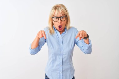 Seçkin bir gömlek ve gözlük takan orta yaşlı bir iş kadını izole edilmiş beyaz arka planda parmaklarını göstererek reklamını, şaşırmış yüzünü ve ağzını açmış.