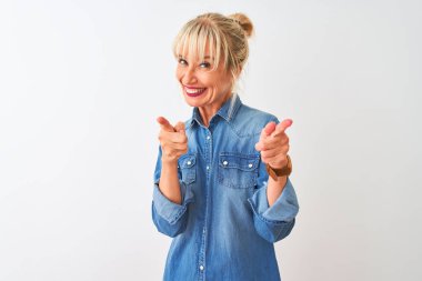 İzole edilmiş beyaz arka plan üzerinde dikilmiş sıradan bir kot giyen orta yaşlı kadın mutlu ve komik yüzlü parmaklarını kameraya doğrultuyor. İyi enerji ve titreşimler.