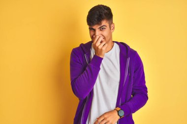 Mor eşofman üstü giyen genç Hintli adam izole edilmiş sarı arka planda duruyor. Pis ve iğrenç bir koku alıyor. Dayanılmaz bir koku. Kötü koku konsepti.