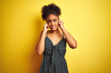 İzole edilmiş sarı arka plan üzerine günlük yeşil elbise giyen Afrikalı Amerikalı bir kadın yüksek sesli müzik sesi için parmaklarıyla kulaklarını kapatıyor. Sağır kavramı.
