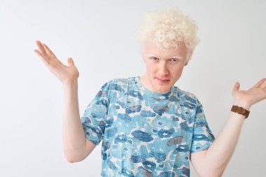 Sıradan tişörtler giyen genç albino bir adam izole edilmiş beyaz arka planda duruyor ve elleri ve kolları havada kafası karışmış bir ifade takınıyor. Şüphe kavramı.