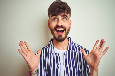 İzole edilmiş beyaz arka plan üzerinde duran çizgili tişörtlü genç adam çılgın ve başarıyı kollarını kaldırıp heyecanla haykırarak kutluyor. Kazanan konsept