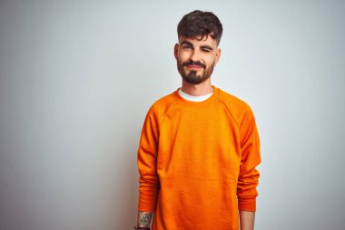 Turuncu süveter giyen genç adam izole edilmiş beyaz arka plan üzerinde duruyor kameraya seksi bir ifadeyle bakıyor, neşeli ve mutlu bir yüzle..