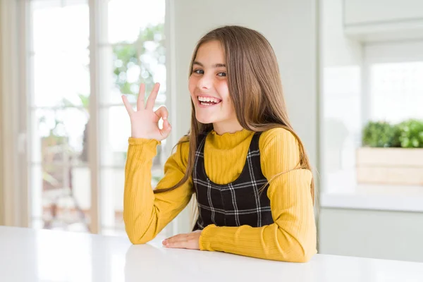 若い美しいブロンドの子供の女の子身に着けていますカジュアルな黄色のセーターに自宅笑顔正行うことでOkサインで手と指 成功した表現 — ストック写真